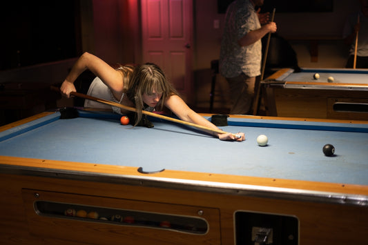 a woman leaning over a pool table with a cue in her hand