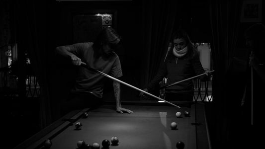 A man and a woman playing pool in a dark room