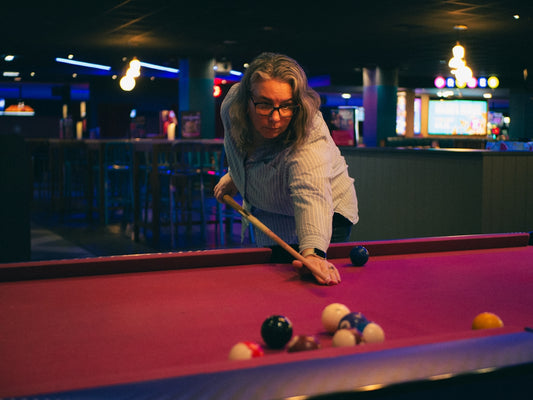 Woman plays pool in a dimly lit pool hall.