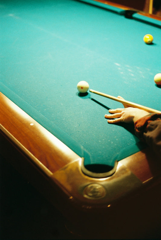 A person plays billiards on a green felt table.