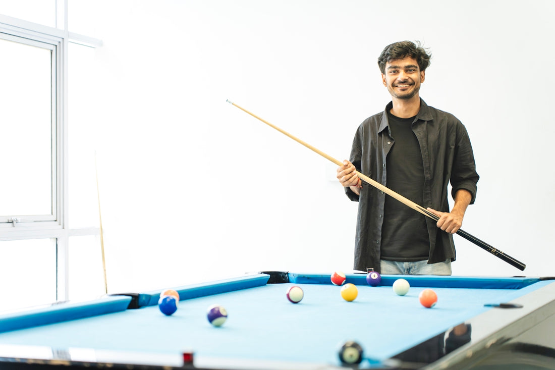 Smiling man holds cue stick by a blue pool table.
